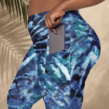 Blue and green tie dye patterned leggings with a pocket holding a phone against a beige background.