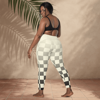 Woman wearing checkered leggings standing against a beige wall with a plant.