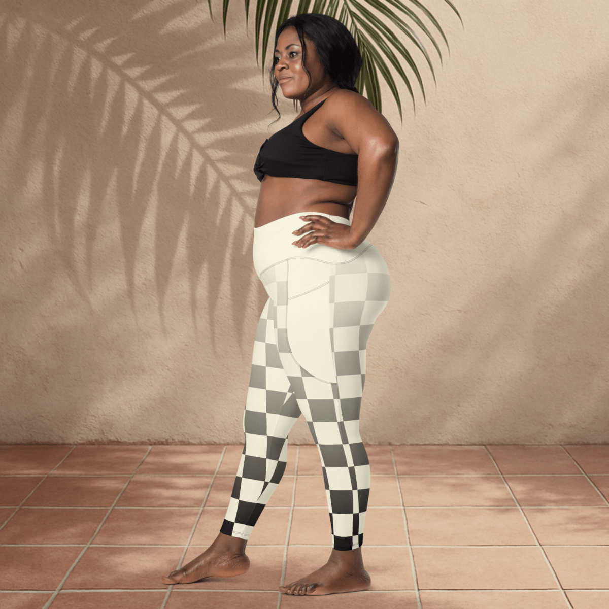 Woman wearing black sports bra and checkered leggings standing against a beige wall.