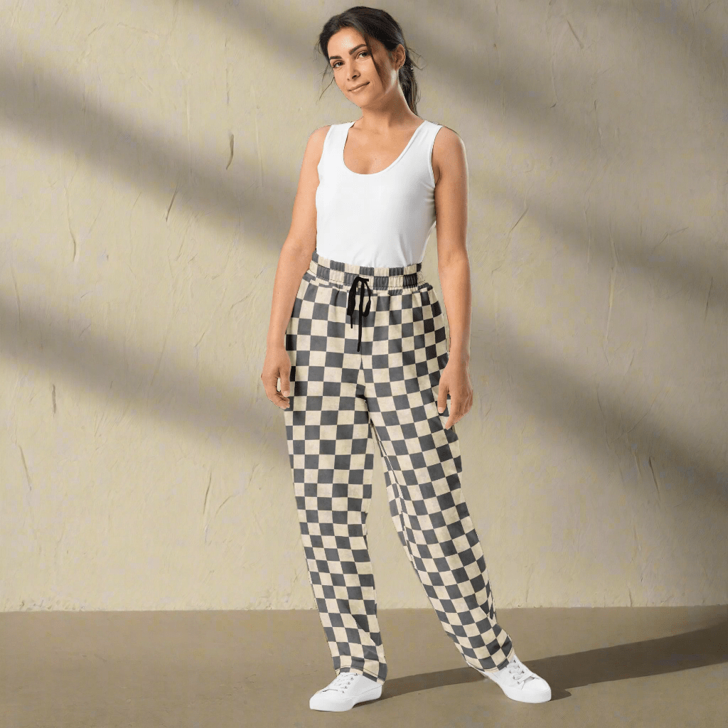 Woman wearing a white sleeveless top and checkered pants against a beige wall.