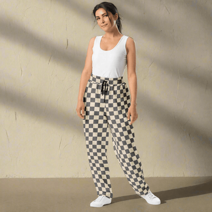 Woman wearing a white sleeveless top and checkered pants against a beige wall.