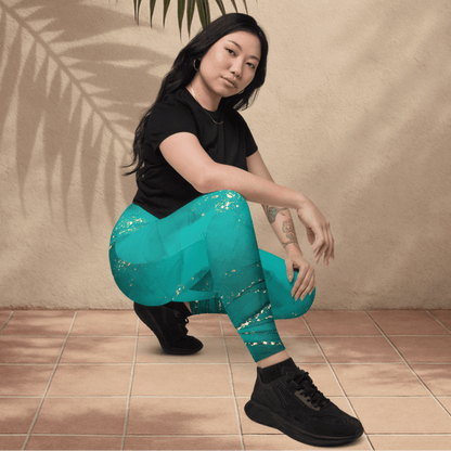 Woman wearing teal leggings with gold patterns and black shoes on a beige background