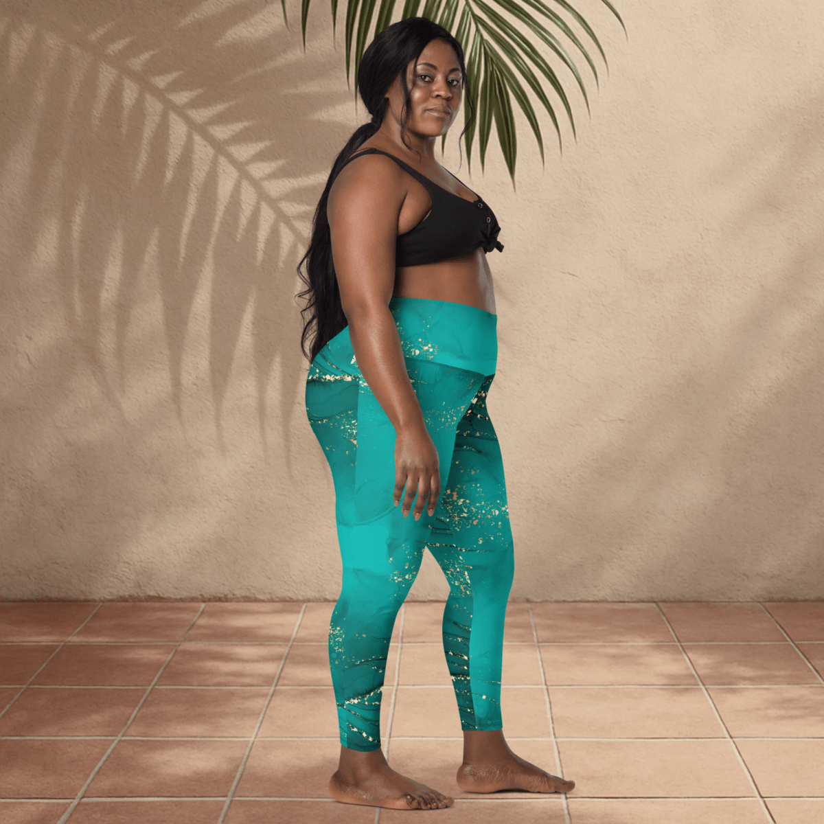 Woman wearing teal leggings with white patterns against a beige wall.