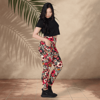 Woman wearing a black top and colorful floral pants standing against a beige wall with a palm leaf.