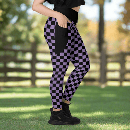 Person wearing black and purple checkered leggings outdoors on a grassy area with a blurred wooden fence in the background.