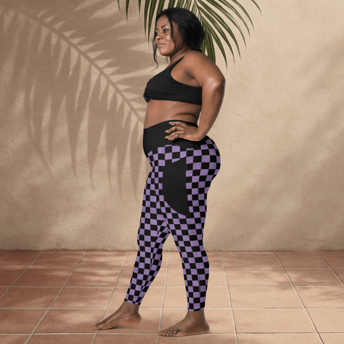 Woman wearing a black sports bra and purple checkered leggings against a beige wall.