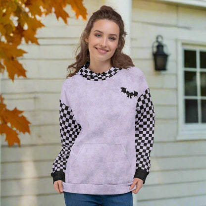 Woman wearing a light purple hoodie with checkered sleeves in front of a house with autumn leaves.
