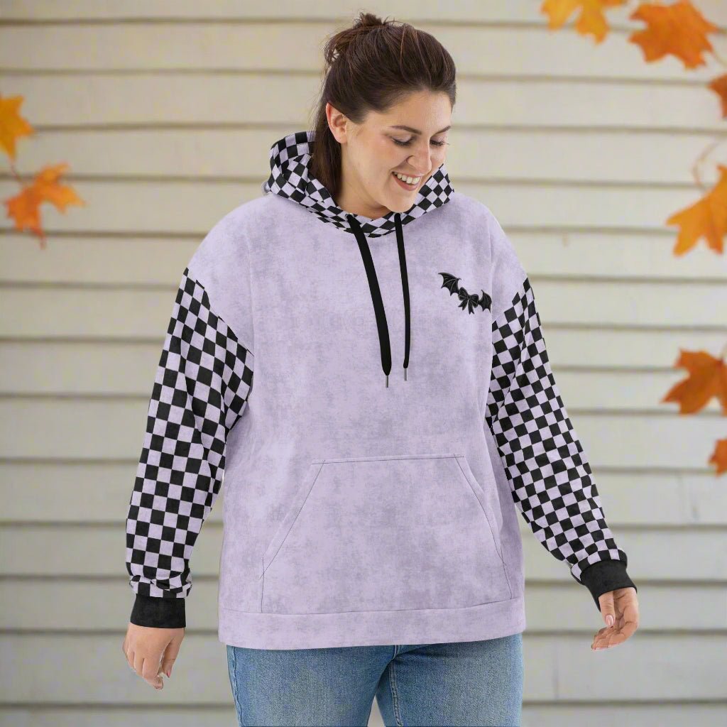 Woman wearing a light purple hoodie with checkered sleeves and a black bat design, standing against a neutral background.