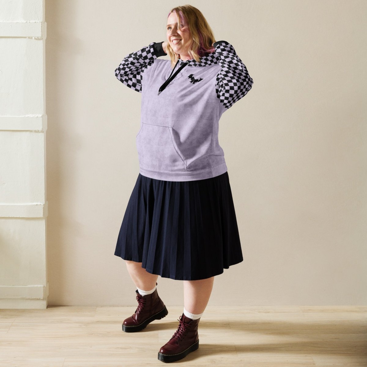 Person wearing a sleeveless purple top with checkered sleeves, black skirt, and maroon boots in a neutral setting.