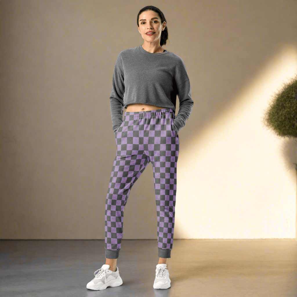Woman wearing a gray long-sleeve top and purple checkered pants on a neutral background