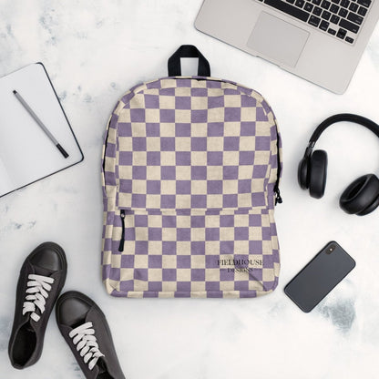 Checkered backpack on a marble surface with a laptop, headphones, and shoes.