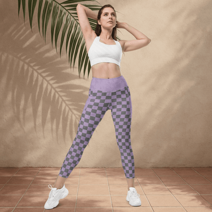 Woman wearing a white sports bra and purple checkered leggings standing against a beige wall with a palm leaf.