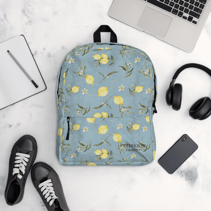 Blue floral backpack with lemons on a white surface with a laptop, headphones, and shoes.