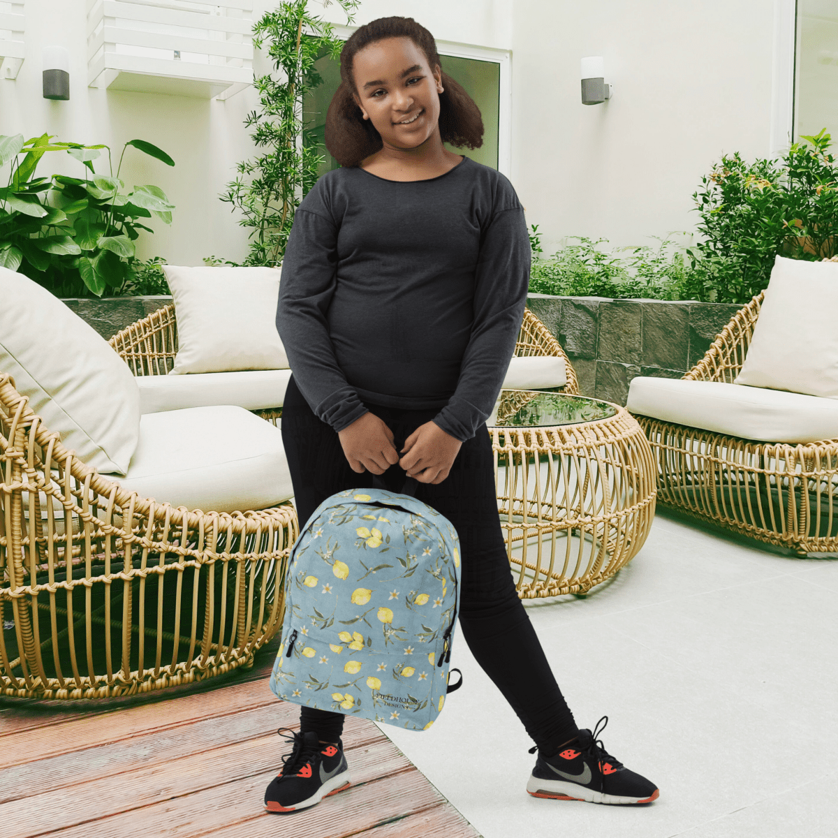 Person holding a blue lemon print backpack in an outdoor setting with wicker chairs and plants.