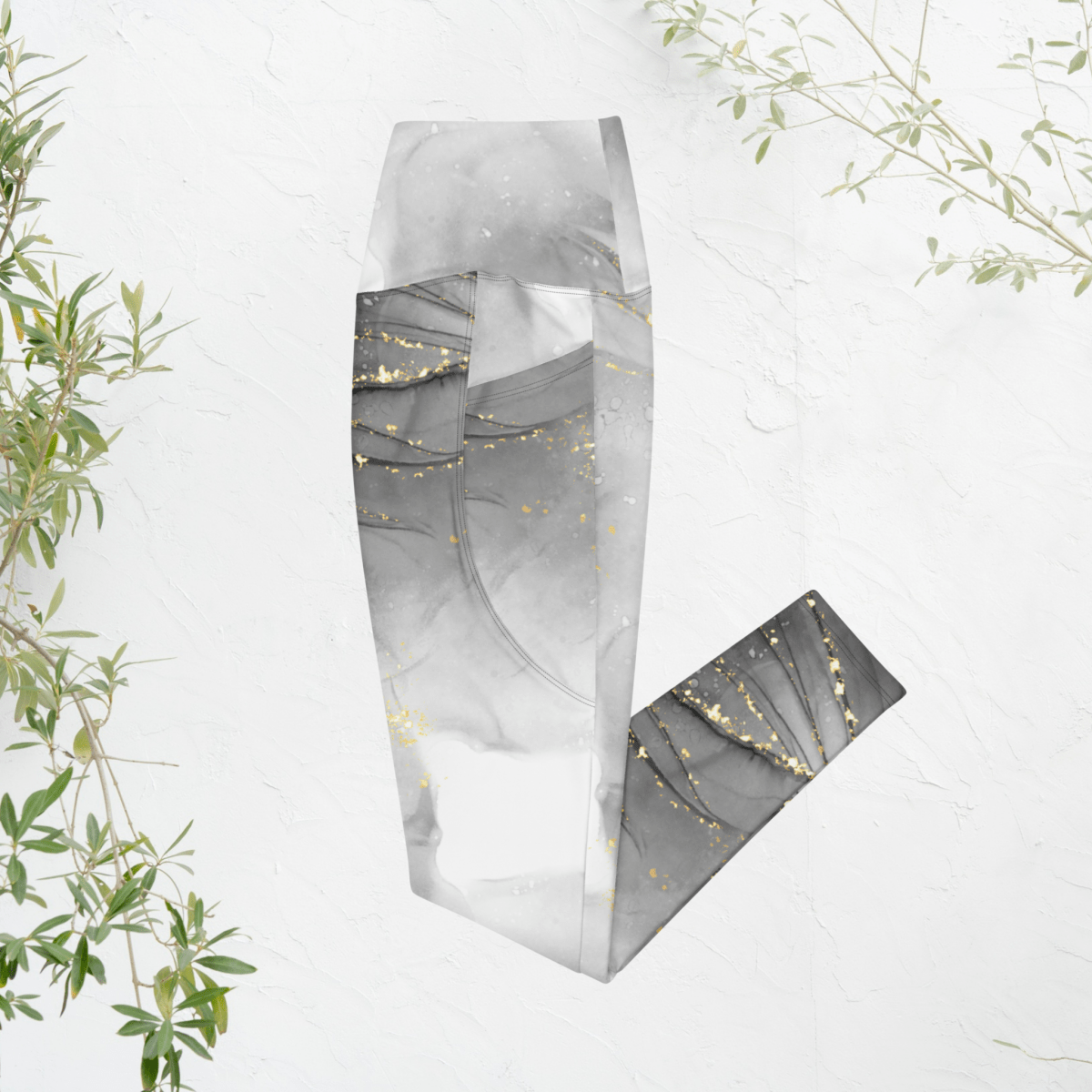 Folded gray and gold leggings on a white background with green leaves.