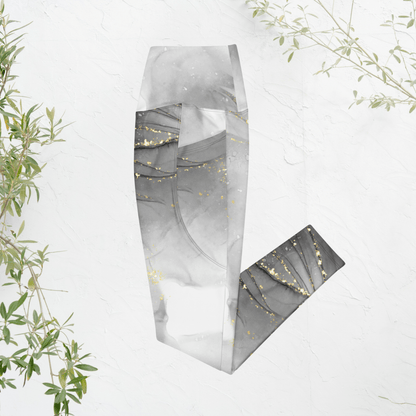 Folded gray and gold leggings on a white background with green leaves.