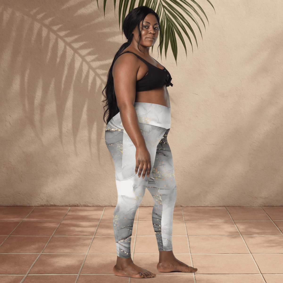 Woman wearing a black sports bra and gray patterned leggings standing against a beige wall.