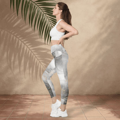 Woman wearing a white sports bra and gray leggings standing against a beige wall with a palm leaf.