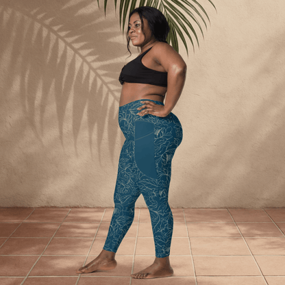 Woman wearing teal floral patterned leggings and black sports bra standing against a beige wall.