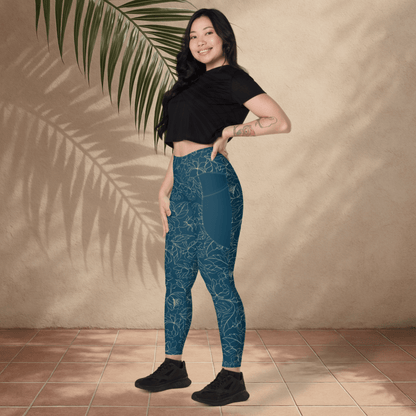 Woman wearing teal floral patterned leggings and black top standing against a beige wall with a palm leaf.
