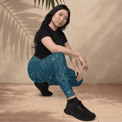 Woman wearing teal floral patterned leggings and black shoes sitting on a tiled floor.