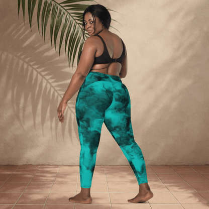 Person wearing teal tie-dye pants standing against a beige wall with a plant.