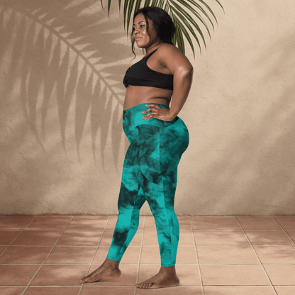 Woman wearing teal patterned leggings and black sports bra standing against a beige wall.