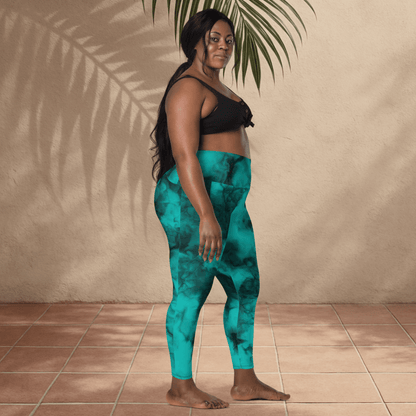 Woman wearing teal patterned leggings and black top standing against a beige wall.