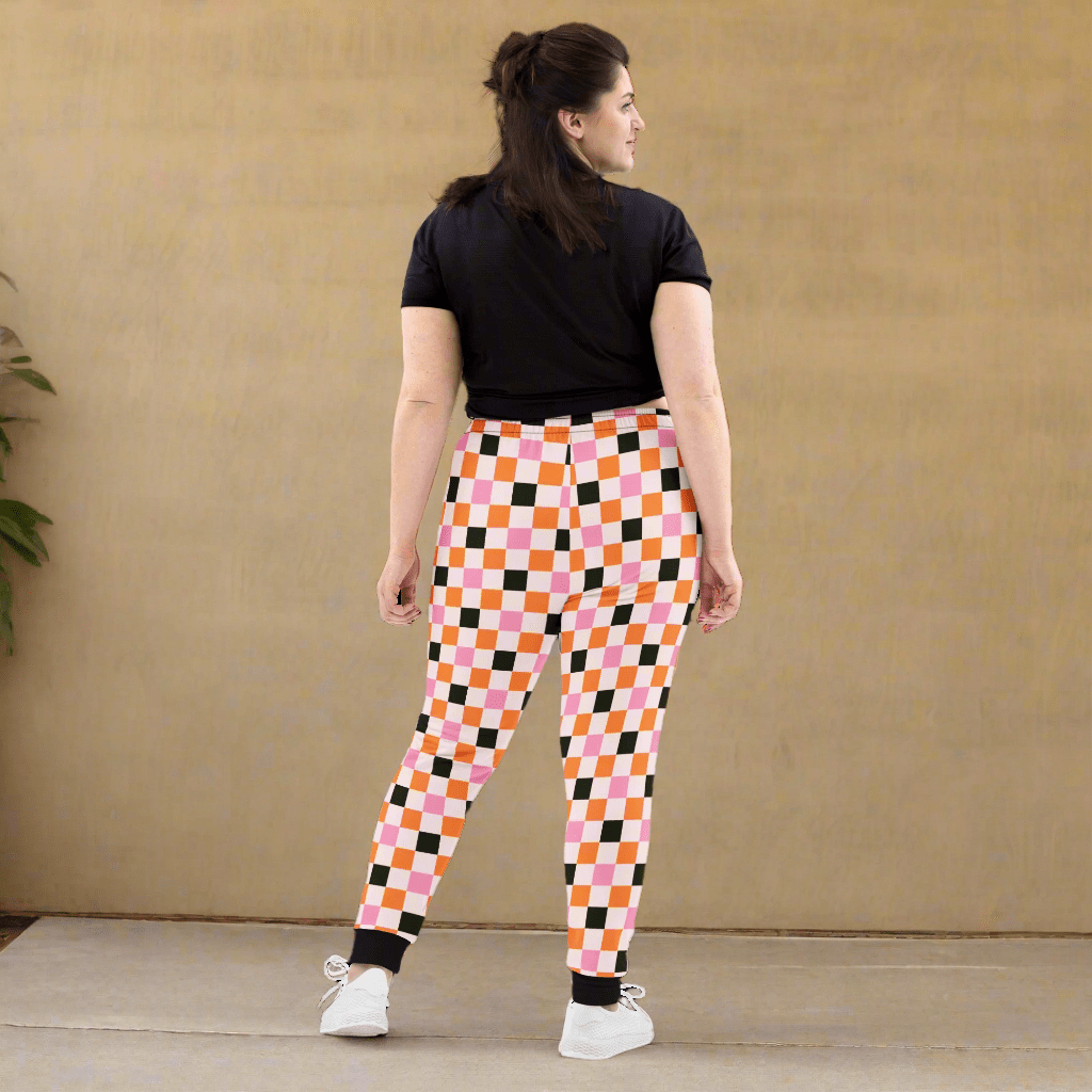 Person wearing colorful checkered pants and a black top against a beige wall.