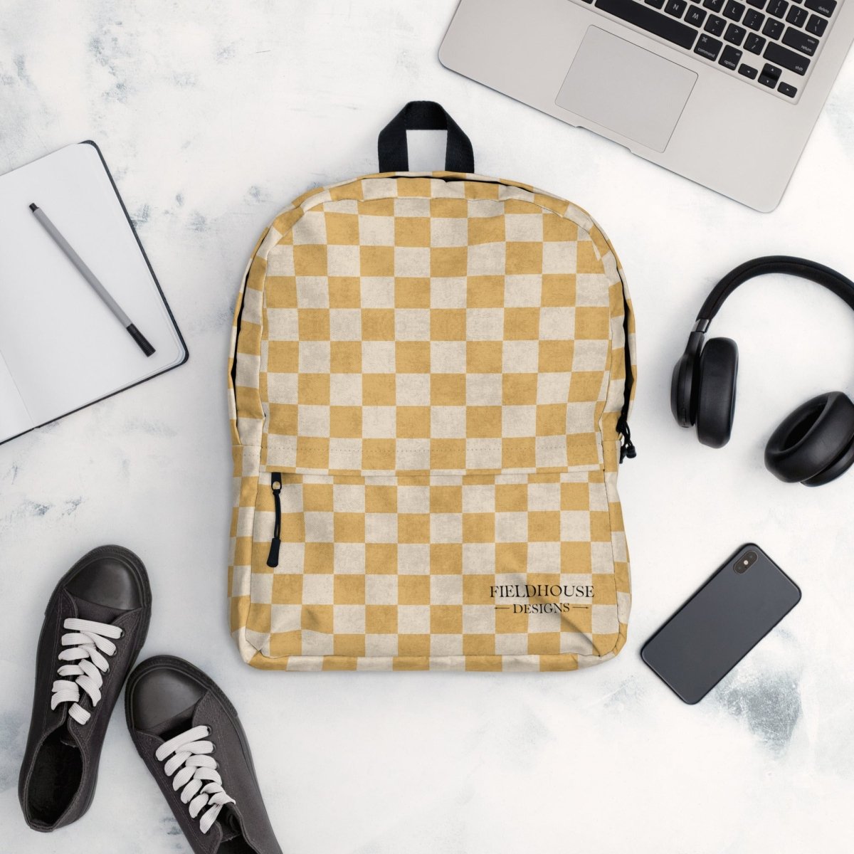 Checkered backpack on a marble surface with a laptop, headphones, and shoes.