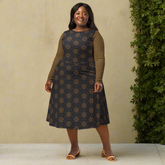 A plus size model wears a navy blue midi dress featuring golden geometric wheel patterns and solid gold sleeves. The dress has a boat neckline, fitted waist, long sleeves, and a flared skirt. She smiles while standing confidently in tan block-heeled sandals against a soft gray studio background.