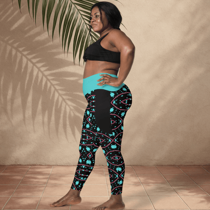 Woman wearing black and teal patterned leggings with a black sports bra against a beige wall.
