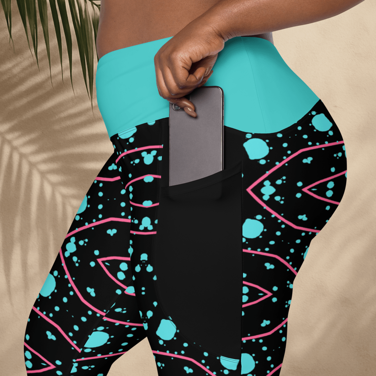 Person wearing black leggings with blue and pink patterns, holding a phone.