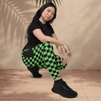 Person wearing black and green checkered pants with a leafy branch above them against a beige wall.