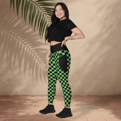 Woman wearing black crop top and green checkered pants standing against a beige wall with a palm leaf.