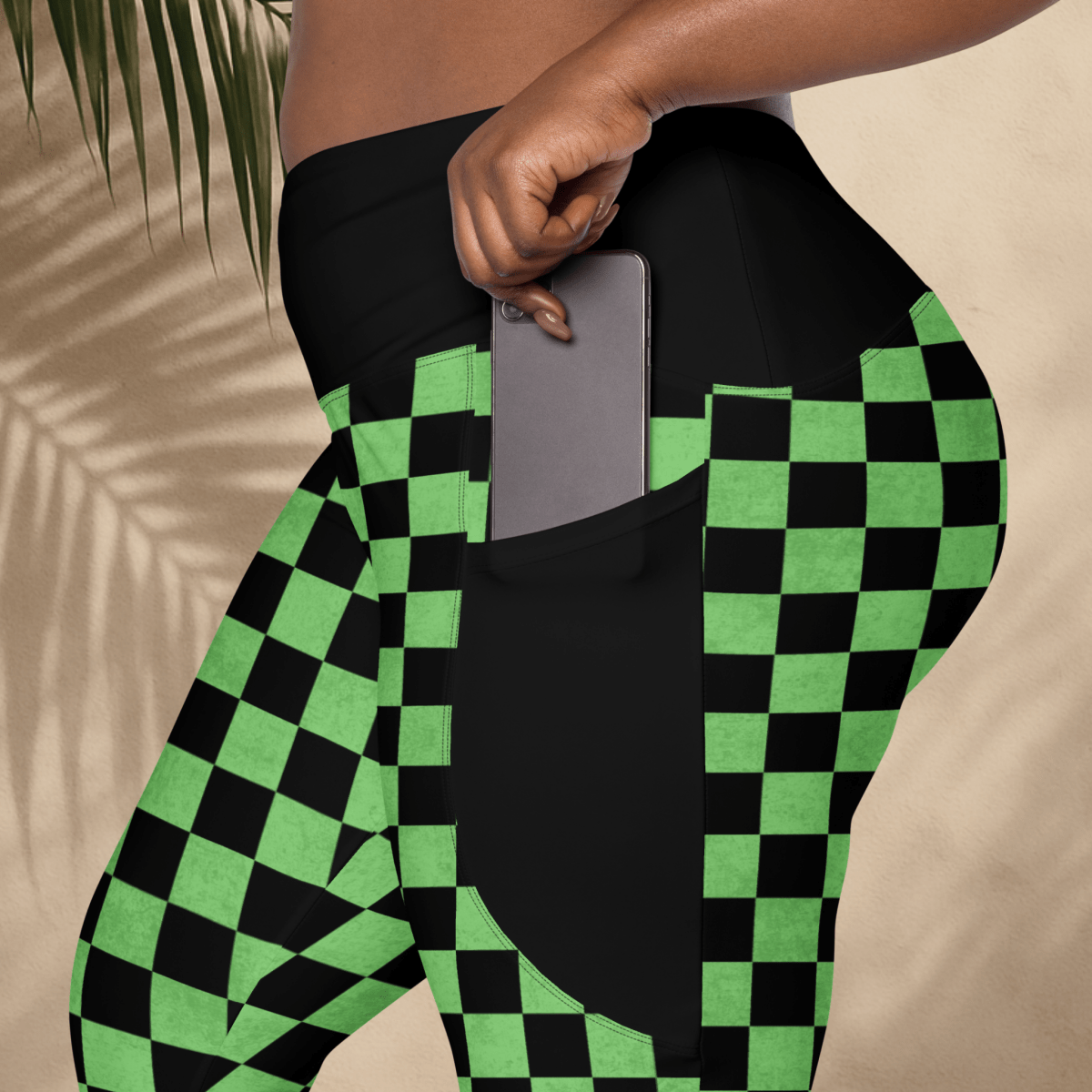 Person wearing black and green checkered leggings with a pocket holding a phone.