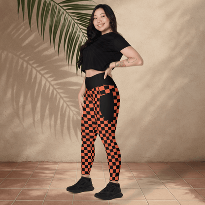 Woman wearing black and orange checkered leggings with a black top against a beige wall.