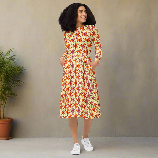 Woman wearing a patterned dress standing against a plain wall with a plant to the left.