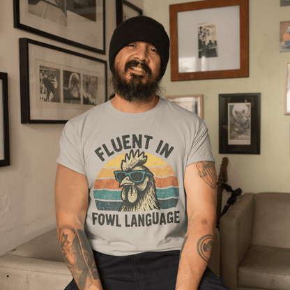 Man wearing a t-shirt with a rooster graphic and text, sitting in a room with framed pictures on the wall.