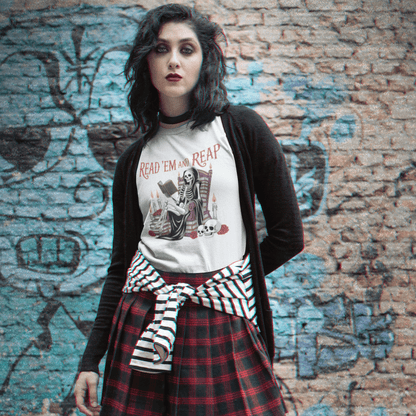 Person wearing a plaid skirt, graphic t-shirt, and black jacket in front of a graffiti-covered brick wall.