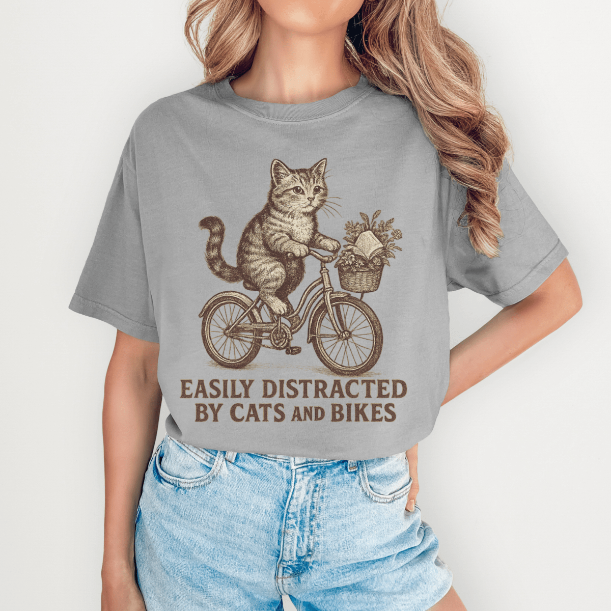 Person wearing a gray t-shirt with a cat riding a bike graphic and text.
