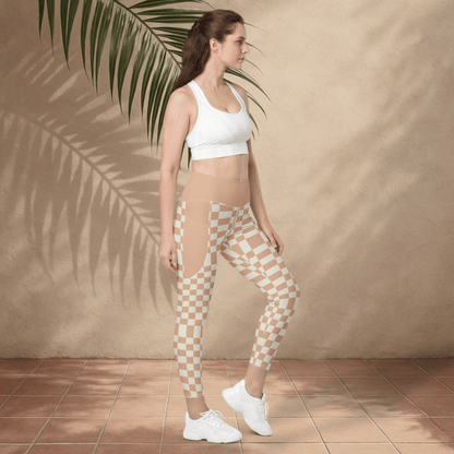 Woman wearing a white sports bra and checkered leggings standing against a beige wall with a palm leaf.