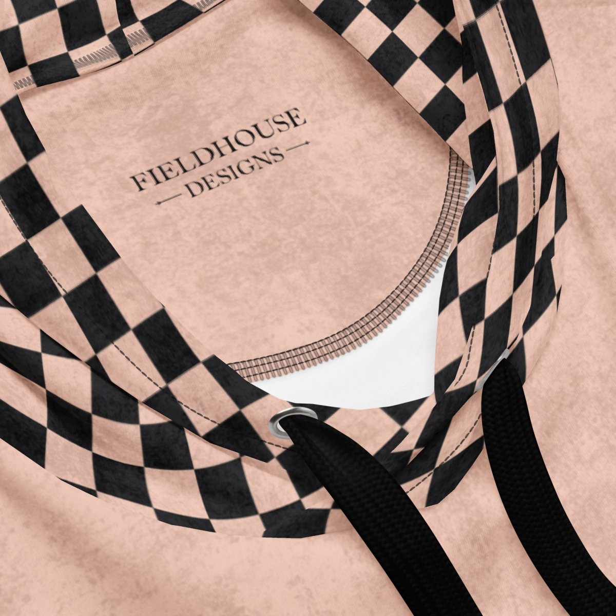 Close-up of a peach hoodie with black checkered pattern and 'Fieldhouse Designs' branding.