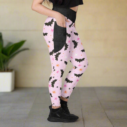 Pink leggings with black bat pattern worn by a person on a neutral background