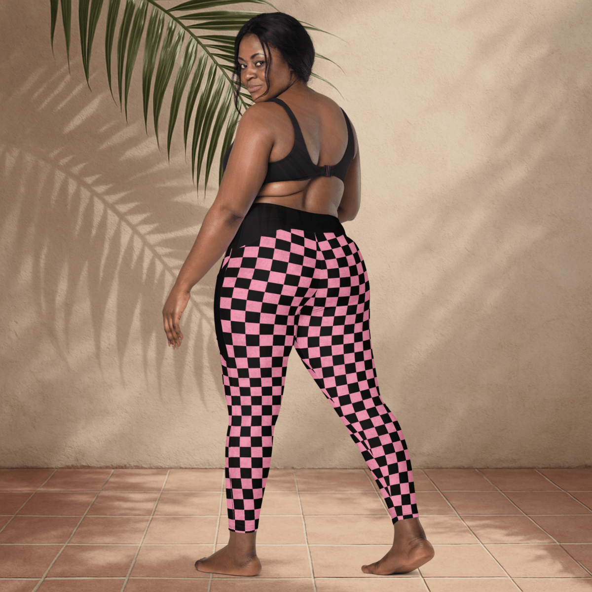Person wearing pink and black checkered pants against a beige wall.