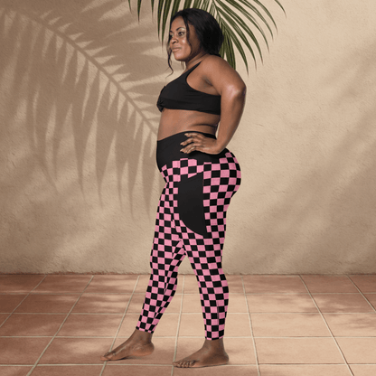 Woman wearing black sports bra and pink checkered leggings standing against a beige wall.
