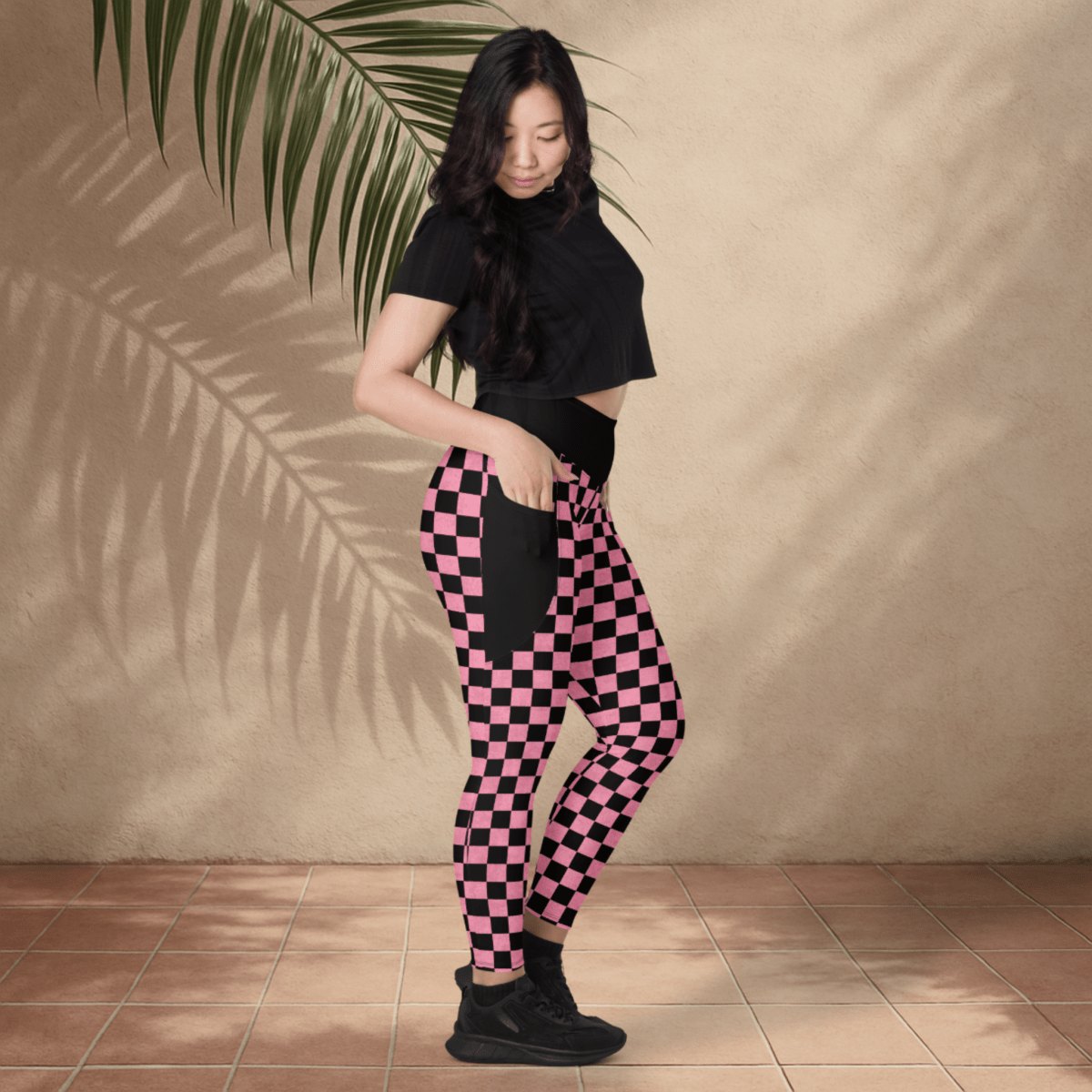 Woman wearing black and pink checkered pants against a beige wall.