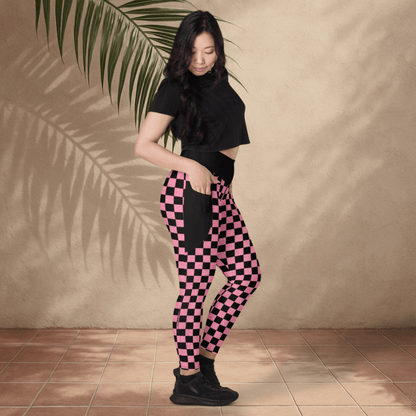 Woman wearing black and pink checkered pants against a beige wall.