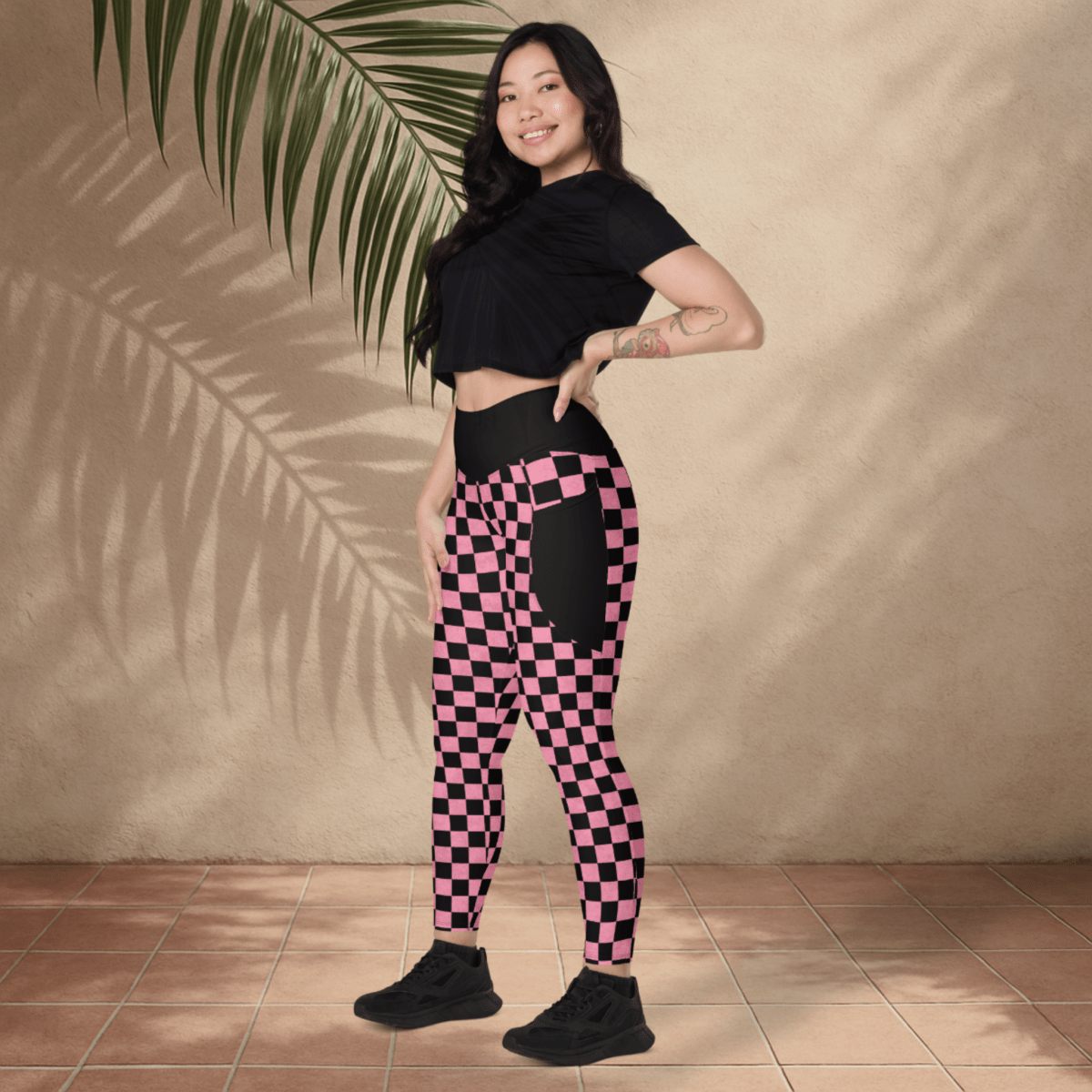 Woman wearing black and pink checkered leggings with a black crop top against a beige wall.