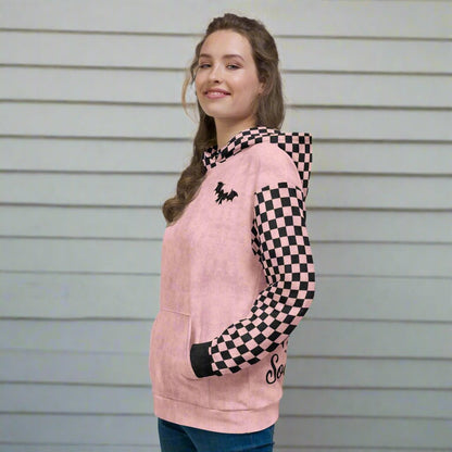 Woman wearing a pink hoodie with checkered sleeves against a gray wall.